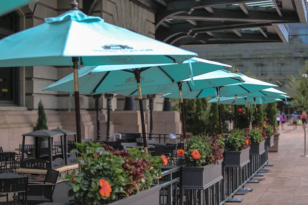 A row of tables and chairs are set up under umbrellas.